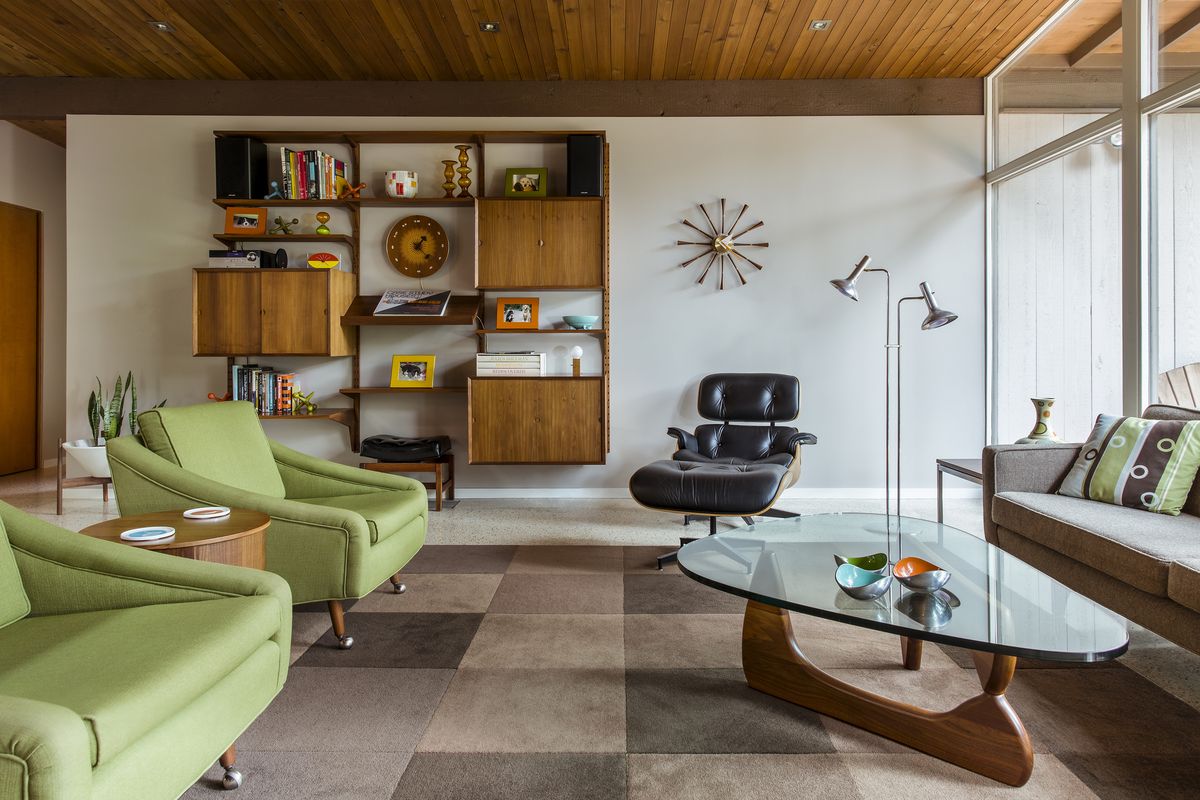 Scene of a midcentury modern style living room with green chairs, checkered area rug, and a oblong coffee table